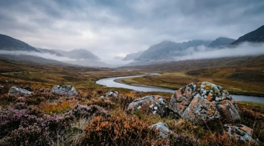 Dramatic Scottish Highland valley shrouded in autumn mist with rugged mountain peaks under moody overcast sky